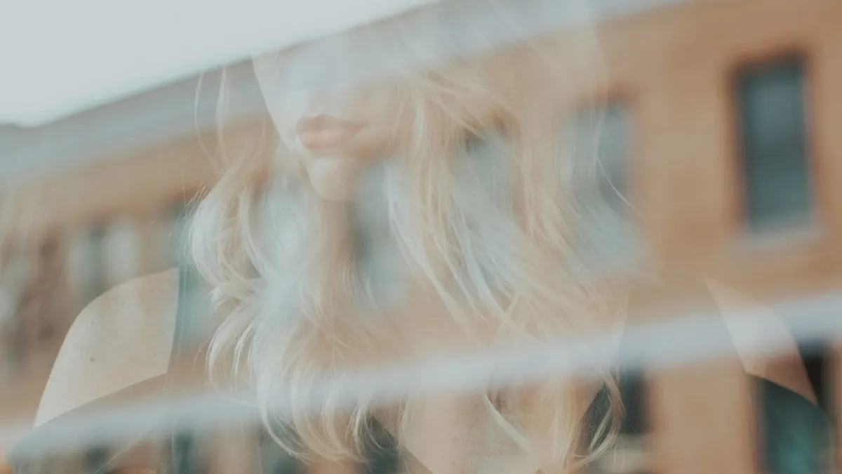 Reflexo suave do rosto de uma mulher no vidro de uma janela, em luz quente, sugerindo o olhar para dentro e a relação consigo mesma.