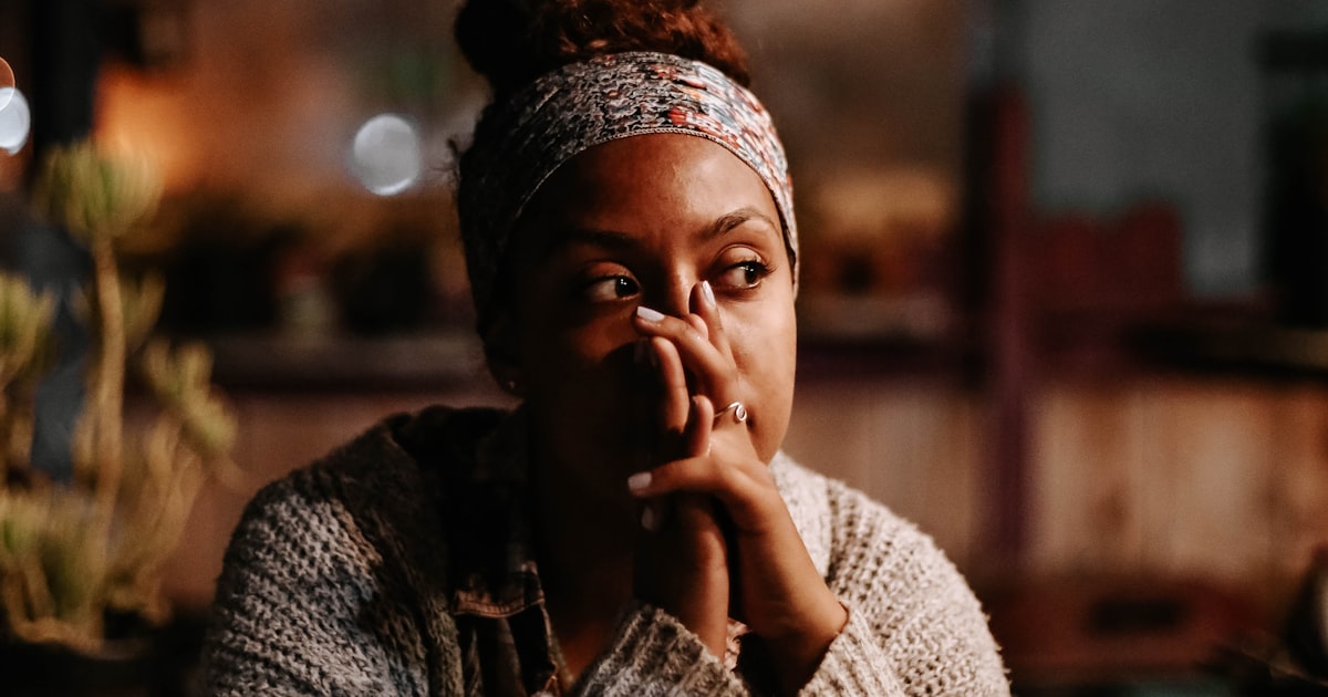 Mulher de expressão serena e cansada, com a mão apoiada perto do rosto, em luz quente e acolhedora, num momento de reflexão sobre o próprio esgotamento