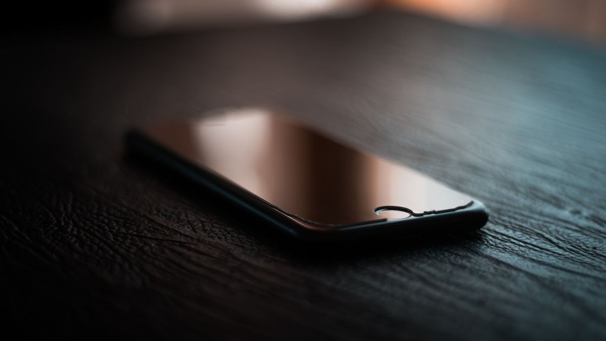 Celular com a tela apagada esquecido sobre uma mesa de madeira, em luz quente de fim de tarde